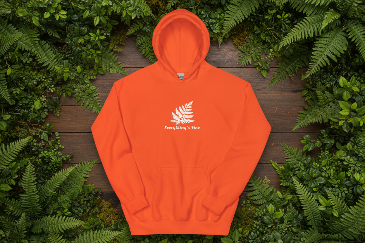 Orange hoodie with enhanced logo and ferns in wooden background